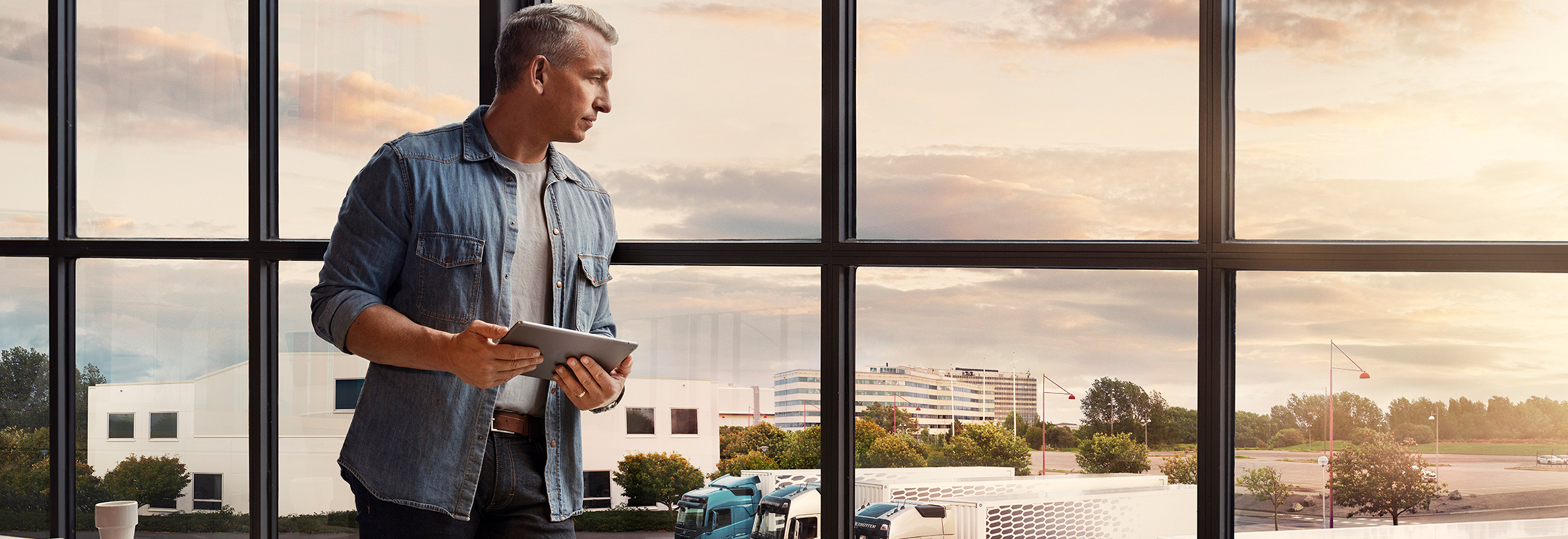 En mand med en tablet står ved et vindue og ser ned over sin lastbilflåde