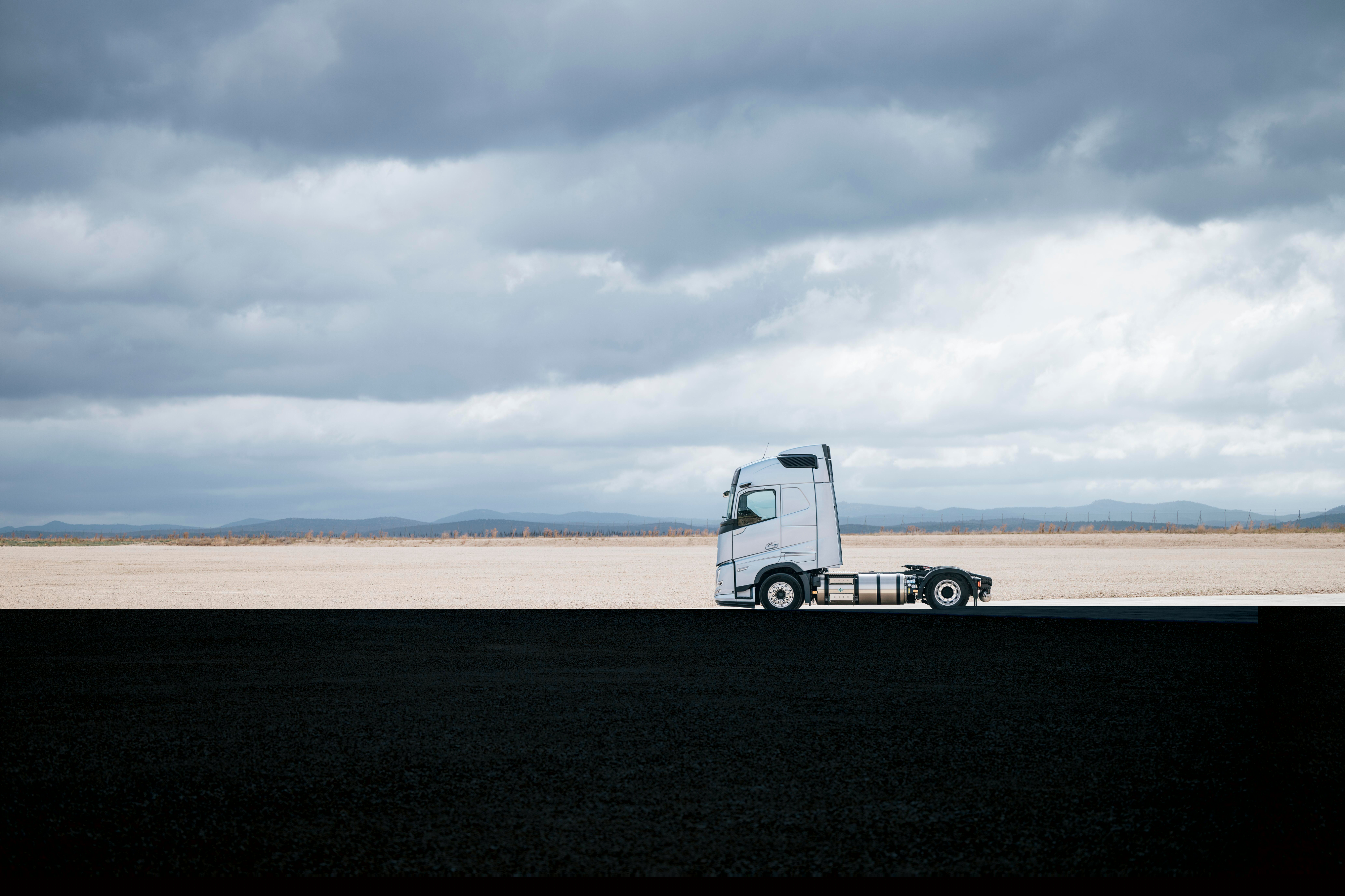 Visning fra siden af en Volvo-lastbil, der er parkeret i et bredt, åbent landskab under en overskyet himmel med vidtstrakte omgivelser og minimalt landskab.